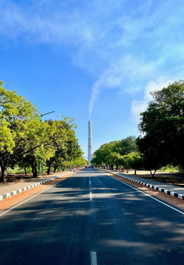 This image beautifully captures a straight, sunlit road lined with vibrant green trees, drawing the eye toward a distant, towering structure. This road symbolizes the journey that every student embarks upon when they decide to pursue higher education, especially abroad. It represents a clear path forward, free from clutter, with a determined destination in sight.